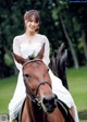 A woman in a white dress riding a brown horse.